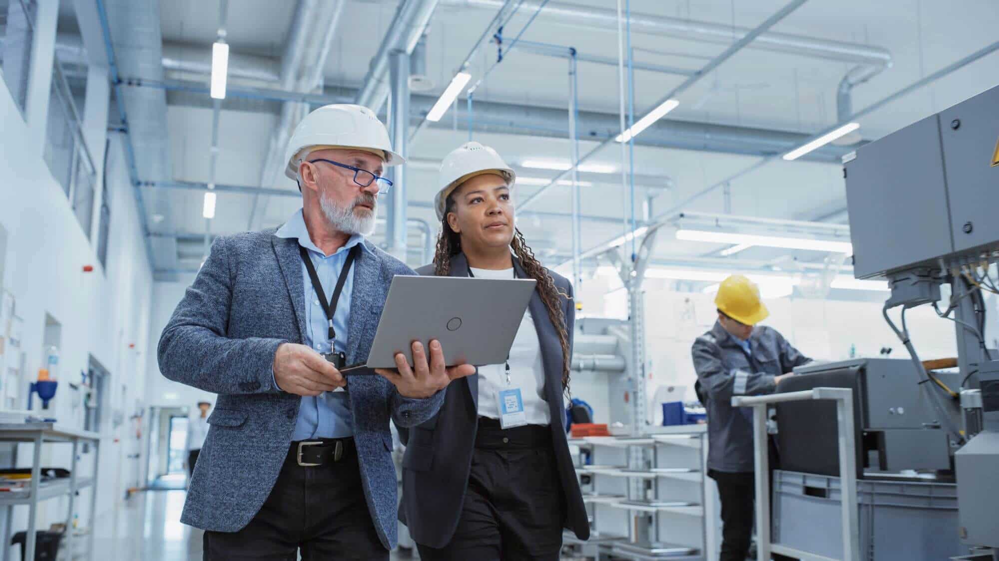 Man and woman walking with hard hats and a laptop